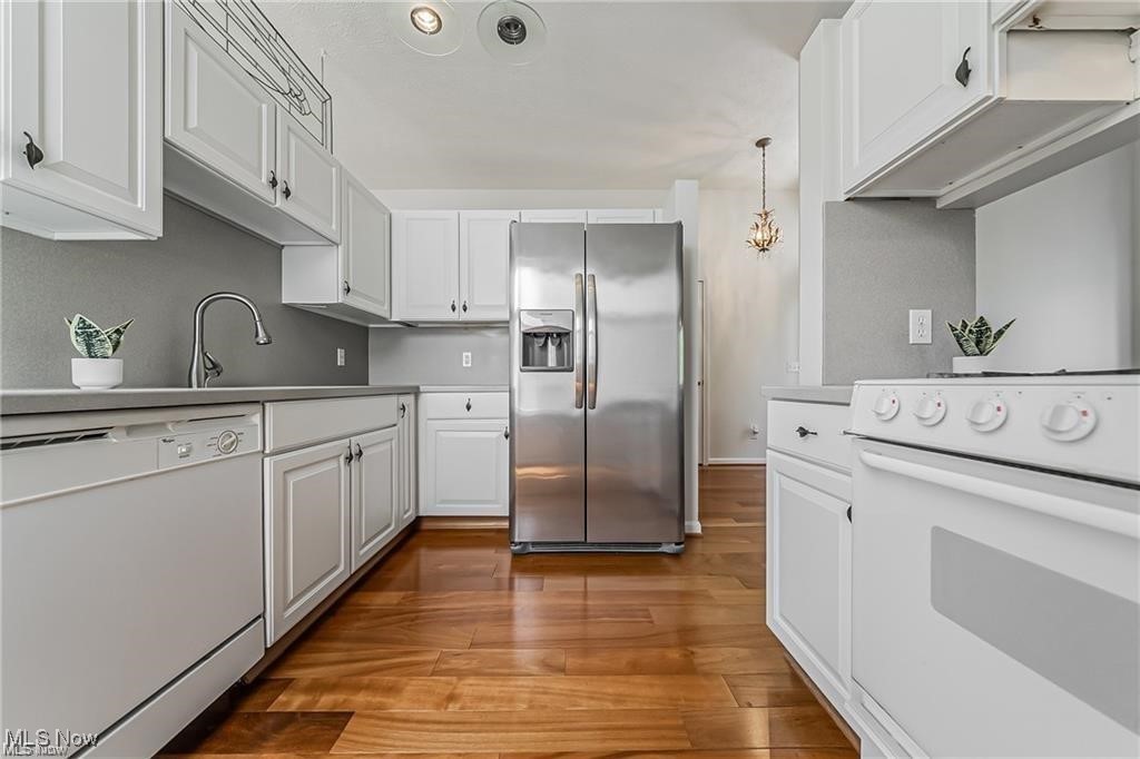 Kitchen with white cabinetry, stainless steel refrigerator, and warm wood flooring.