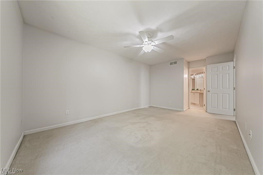 Empty carpeted bedroom with a ceiling fan and open doorway to a vanity area.