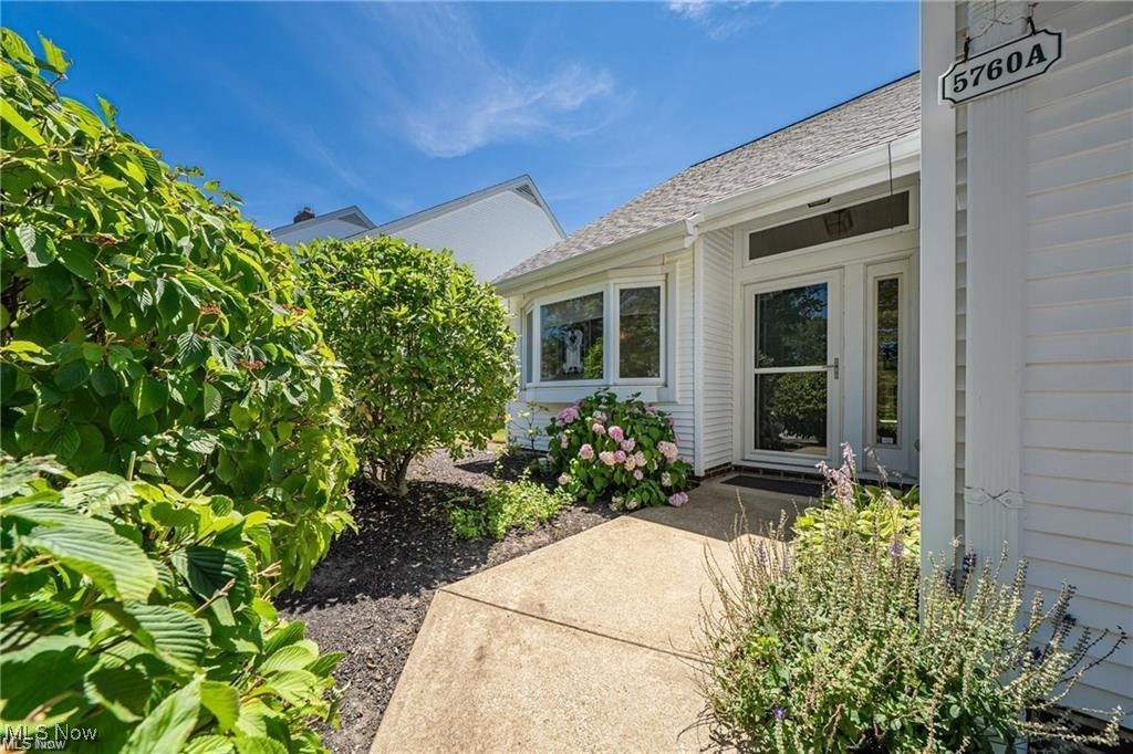 White-sided home entrance with a concrete walkway, flowering shrubs, and a 5760 A address plaque.