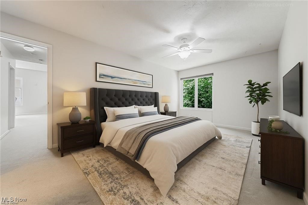 Staged bedroom with a tufted headboard, ceiling fan, wall-mounted TV, and leafy views through the window.