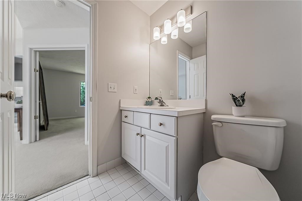 Bathroom with a white vanity, large mirror, tiled floor, and toilet beside an open doorway.