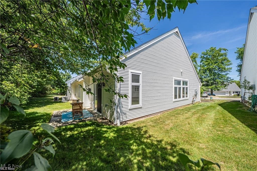 White-sided home with a small patio and chair beside a shaded lawn.