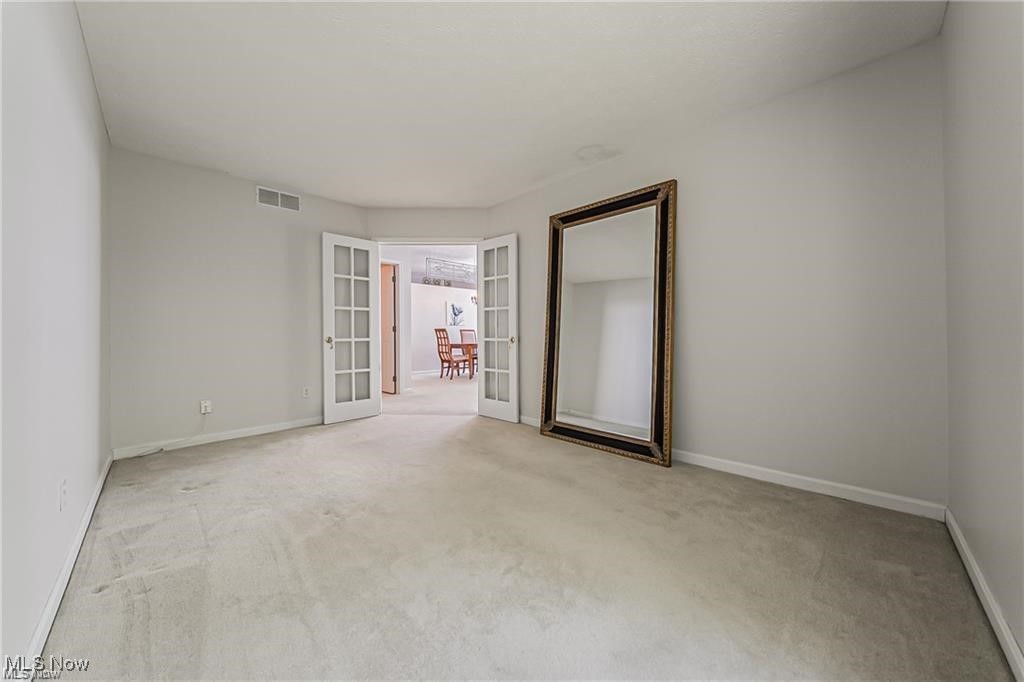 Empty carpeted room with open French doors and a large leaning mirror.