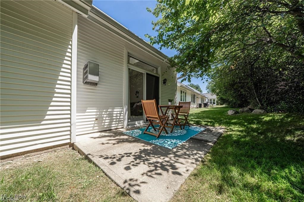 Side patio with a wooden table and chairs beside a white-sided home.