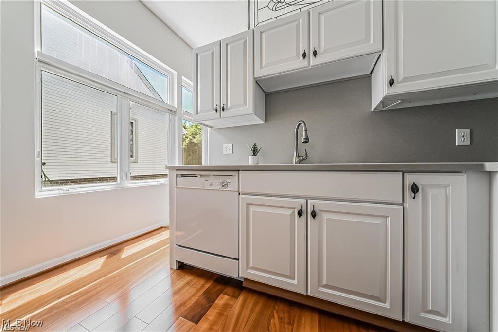 Kitchen with white paneled cabinets, a built-in dishwasher, and wide windows overlooking a neighboring building.