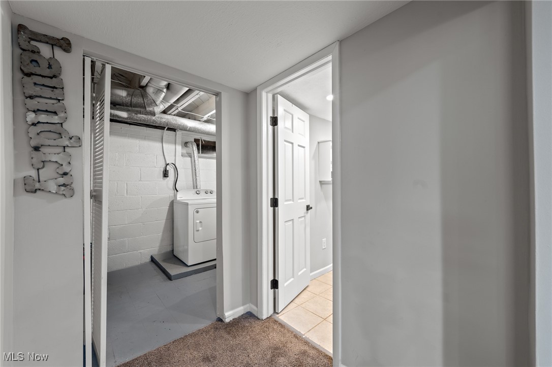 Laundry area with a white dryer, exposed ceiling pipes, and an open doorway to a tiled room.