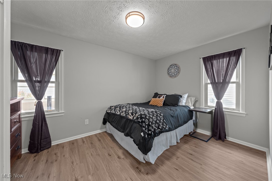 Bedroom with dark curtains, a patterned bedspread, and wood-look flooring.