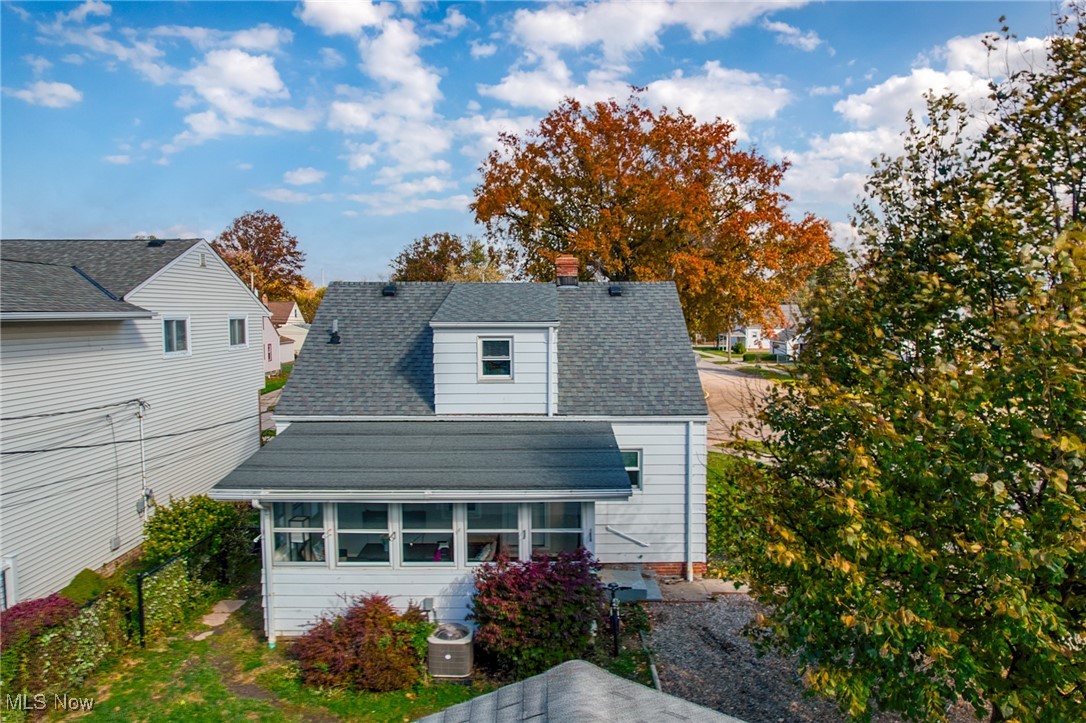 Rear of a white-sided house with an enclosed porch, gravel drive, and autumn trees.