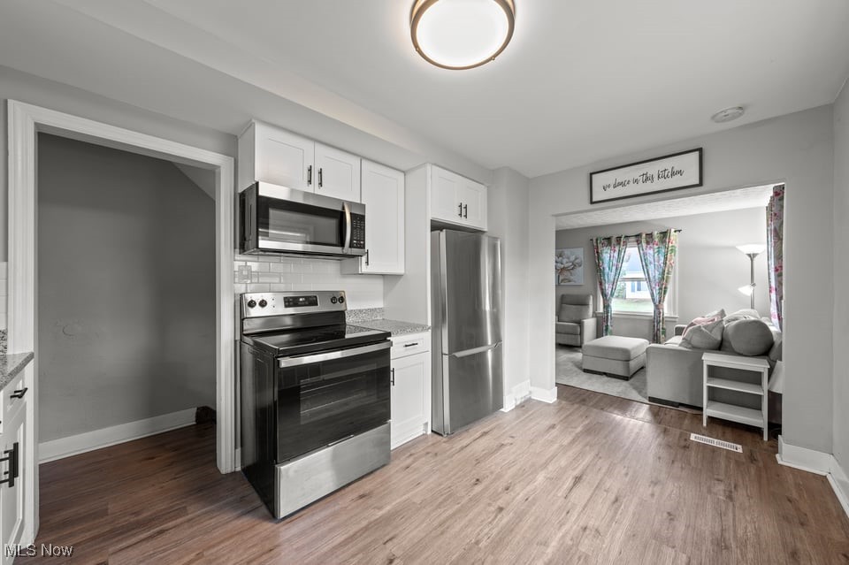 Kitchen with white cabinets and stainless steel appliances, opening into a furnished living room.