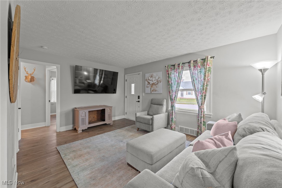 Living room with a gray sectional, ottoman, wall-mounted television, and floral curtains.