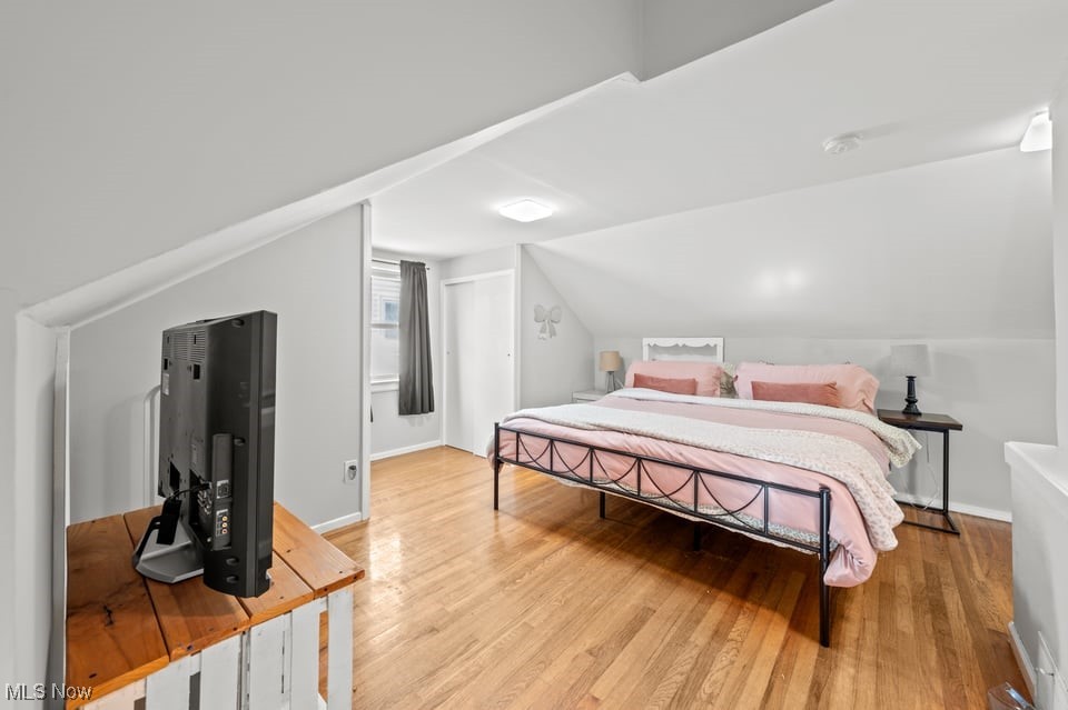Attic bedroom with pink bedding, hardwood floors, and a television on a wooden dresser.