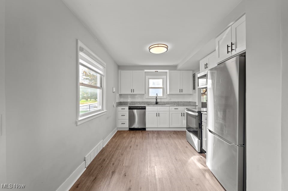 Kitchen with white cabinets, stainless steel appliances, patterned countertops, and wood-look flooring.