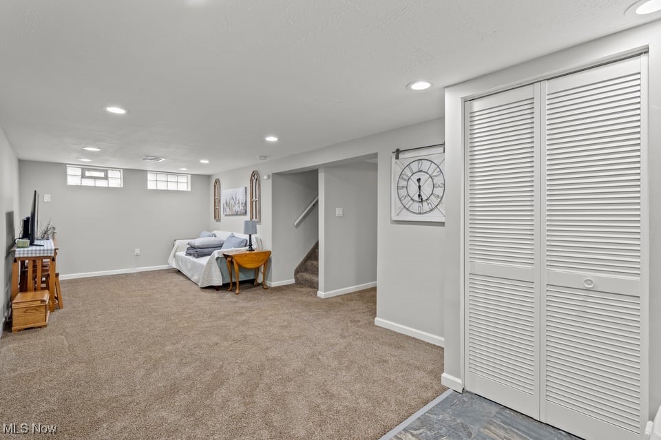 Finished basement room with beige carpet, a bed, stairs, and white louvered closet doors.