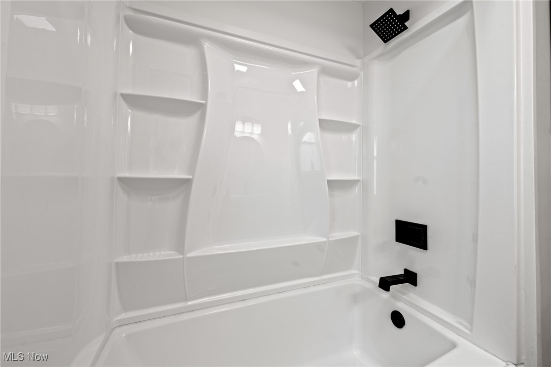 White tub and shower with built-in shelves and black fixtures.