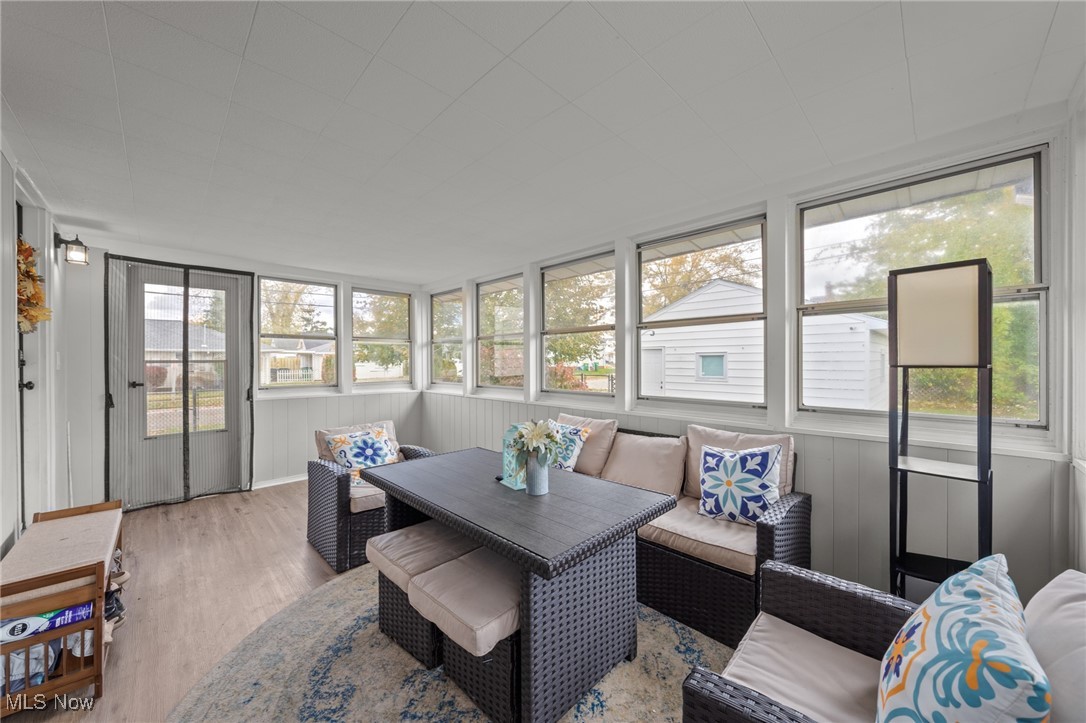 Furnished enclosed sunroom with dark wicker seating, patterned pillows, and windows on two sides.