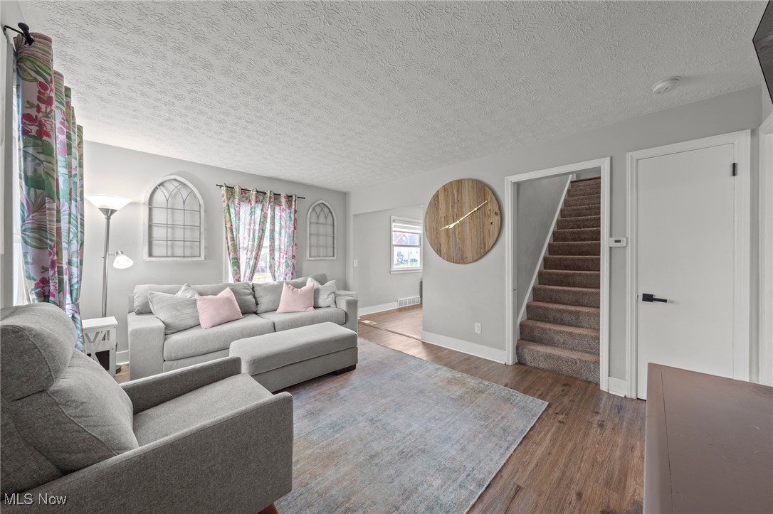 Living room with gray sofas, pink pillows, floral curtains, and a staircase.