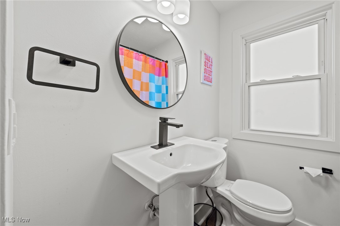 Bathroom with a pedestal sink, round mirror, toilet, and colorful checkered shower curtain.