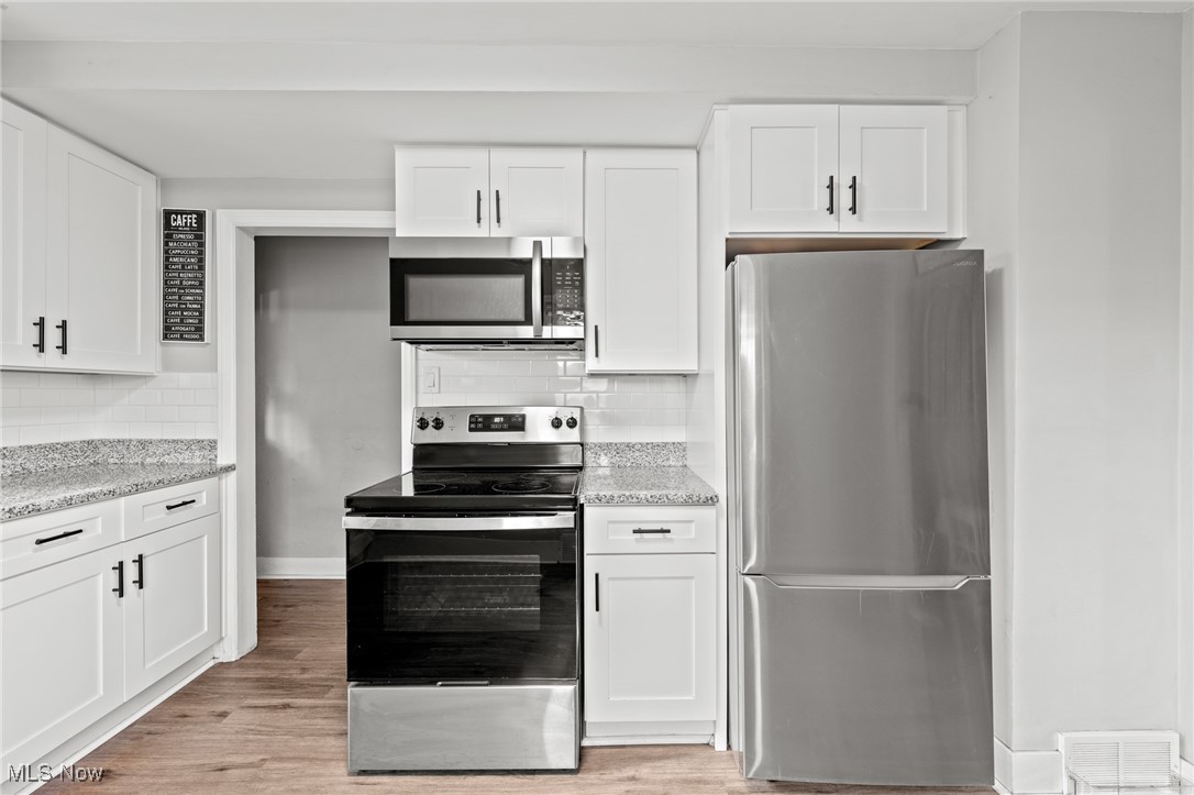 Kitchen with white shaker cabinets, stainless appliances, subway tile backsplash, and speckled countertops.