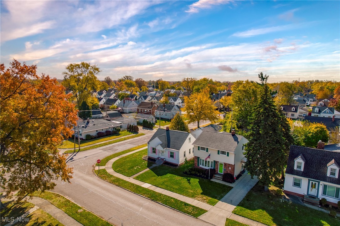 White house on a green corner lot, surrounded by autumn trees and neighborhood homes.
