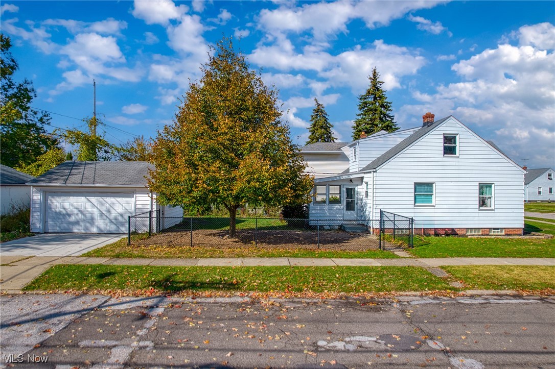White-sided house with a detached garage, chain-link fence, and large autumn tree in the front yard.