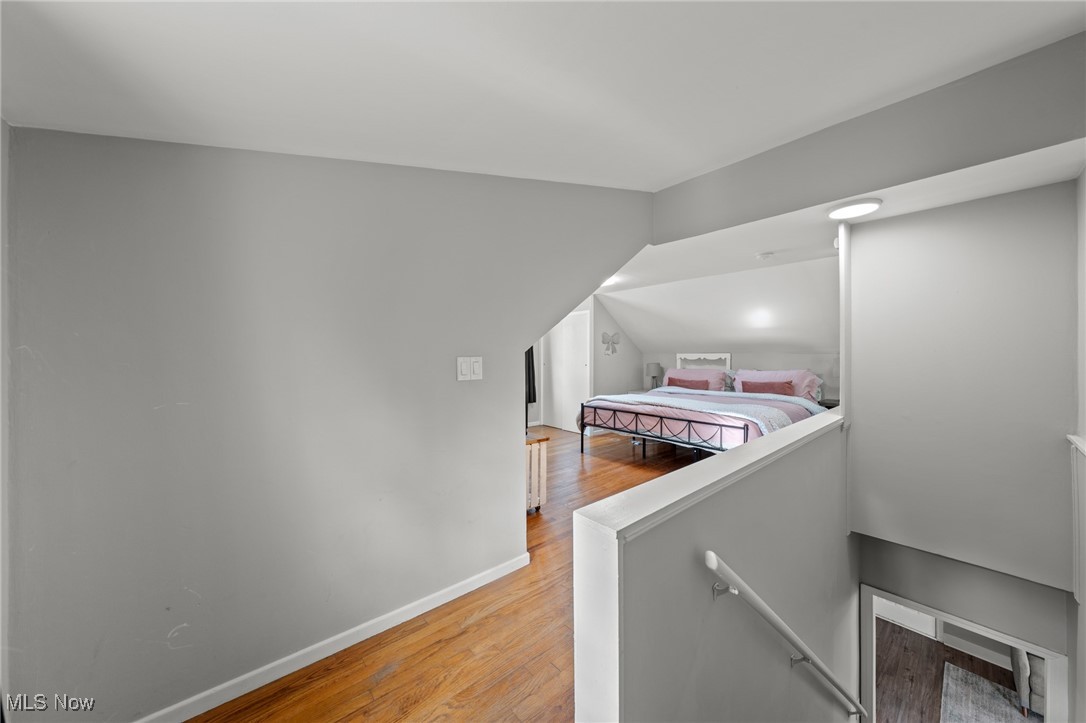 Upstairs bedroom with pink bedding, a sloped ceiling, and hardwood floors, viewed from the landing.