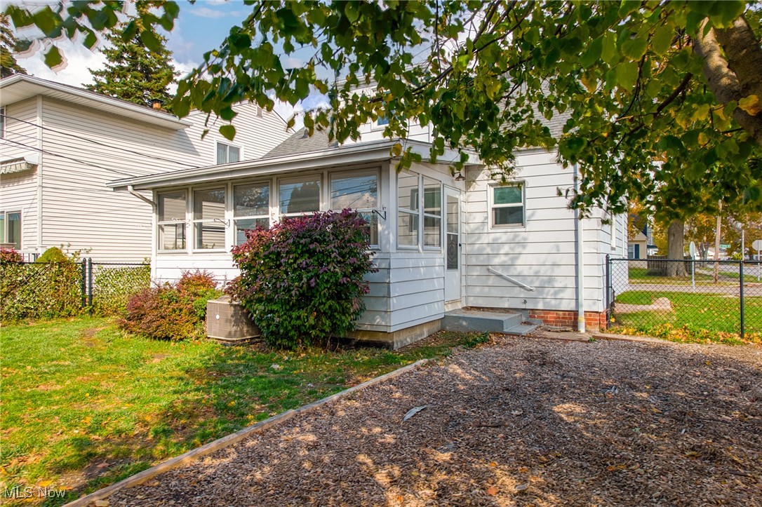White-sided home with an enclosed porch, gravel yard, and chain-link fencing.