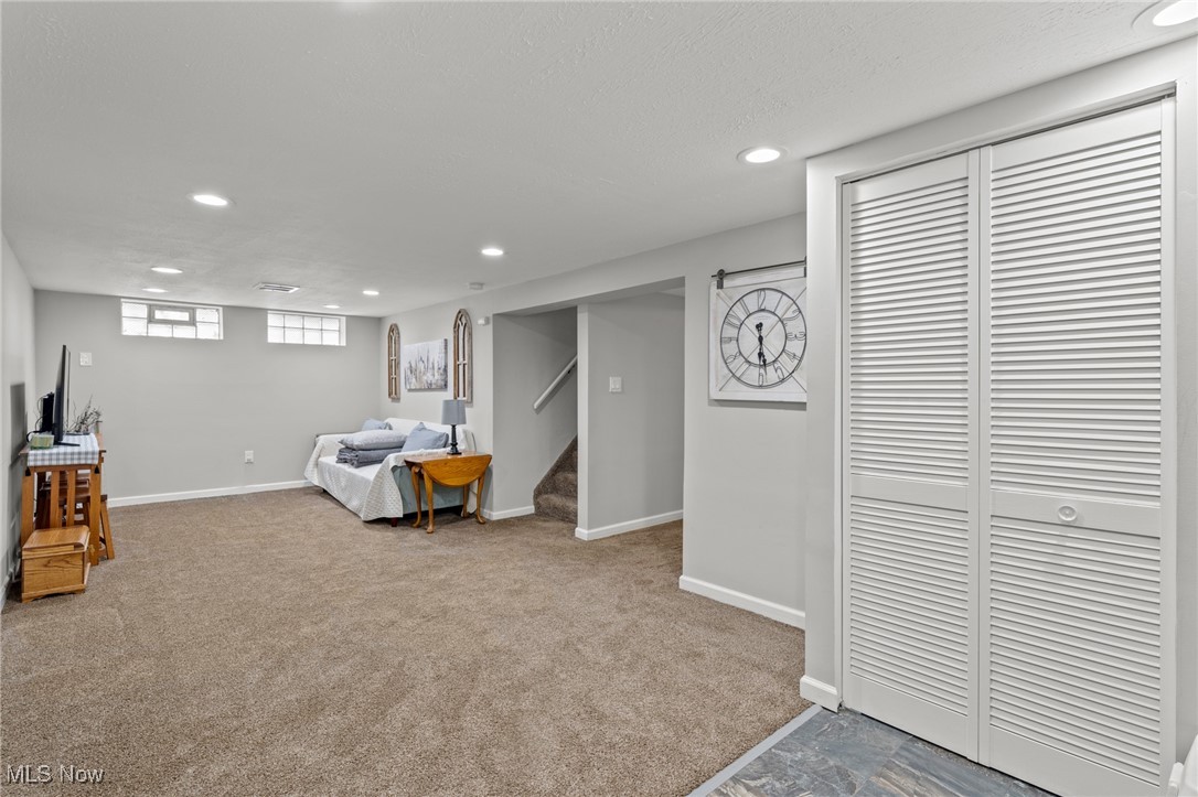 Carpeted lower-level living room with a sofa, small table, stairs, and louvered closet doors.