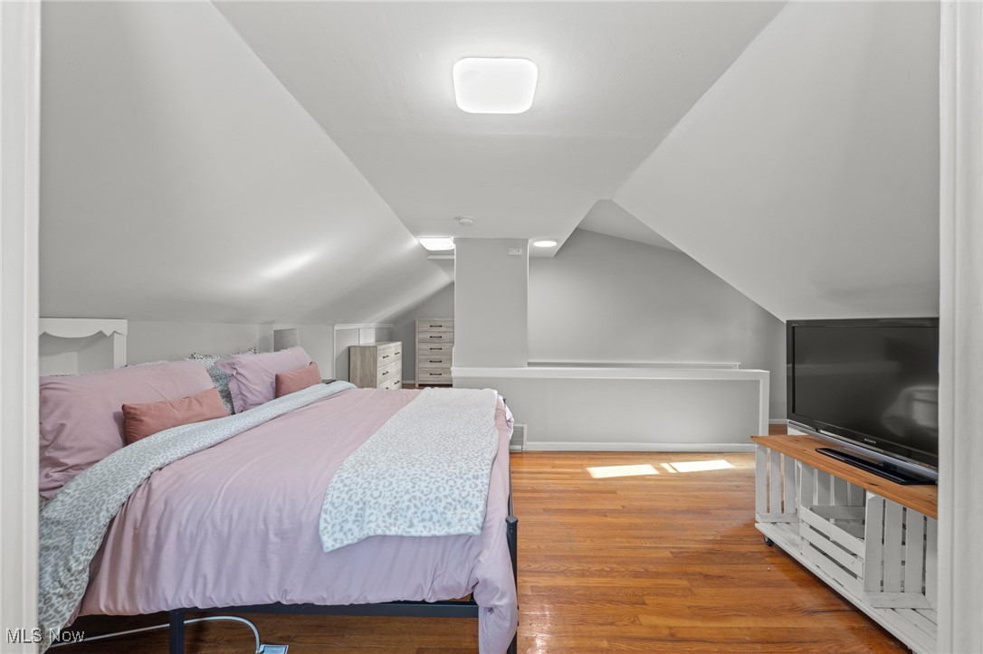 Attic bedroom with pink bedding, sloped ceilings, hardwood floors, and a television.
