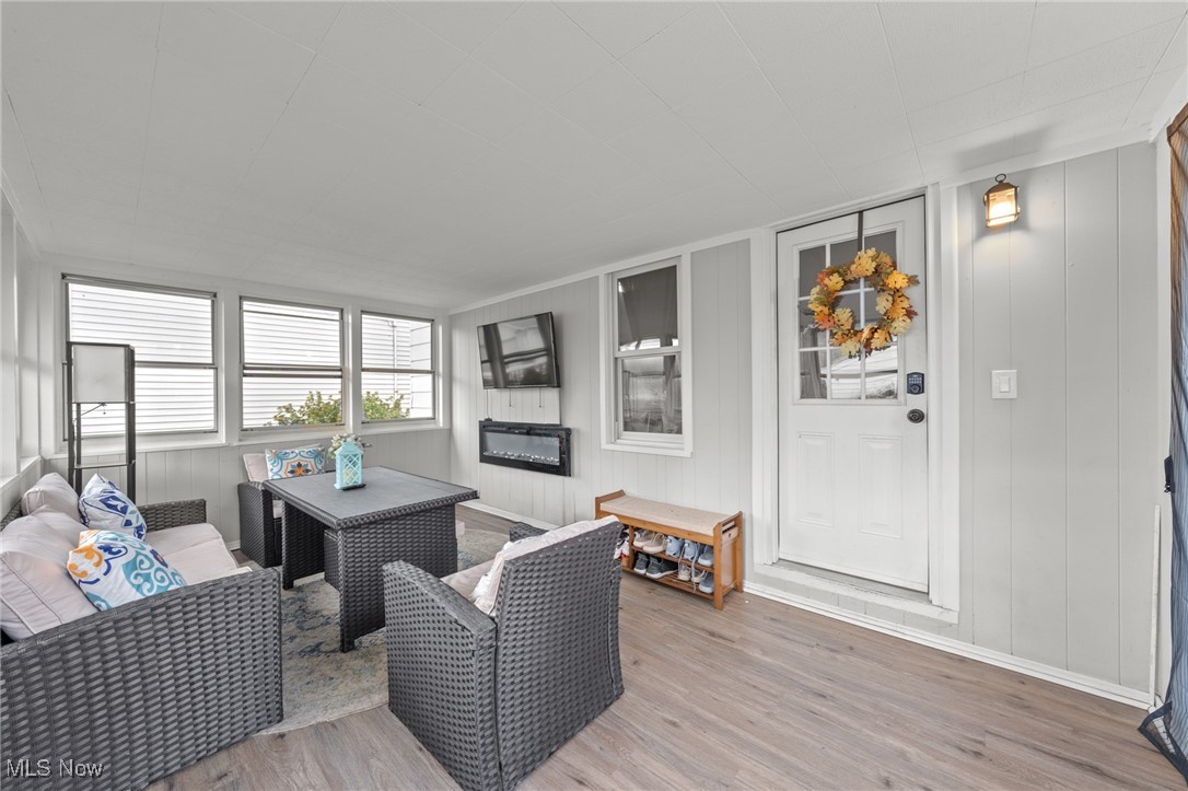 Enclosed porch with gray wicker seating, multiple windows, and a white door with an autumn wreath.