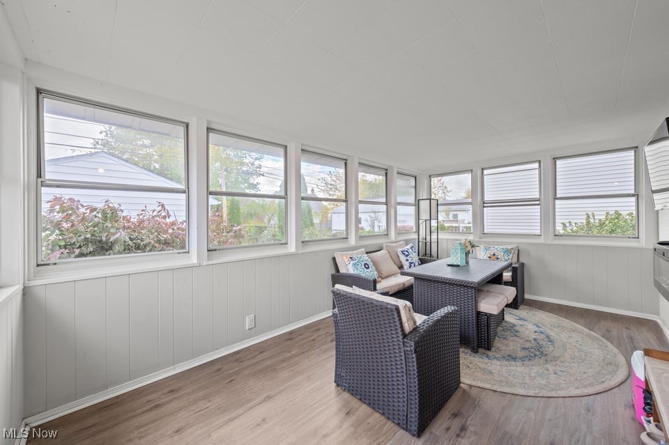 Enclosed sunroom with wraparound windows, wicker seating, and a patterned area rug.