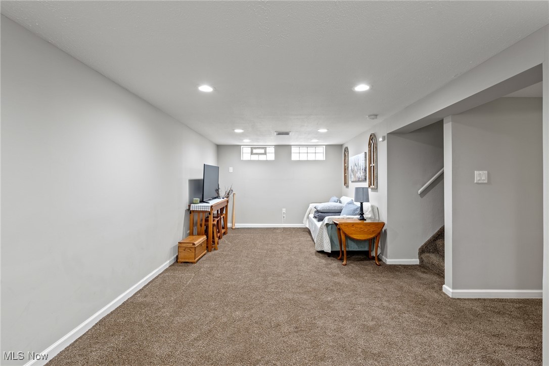 Basement recreation room with carpet, sofa, TV console, and stairs.