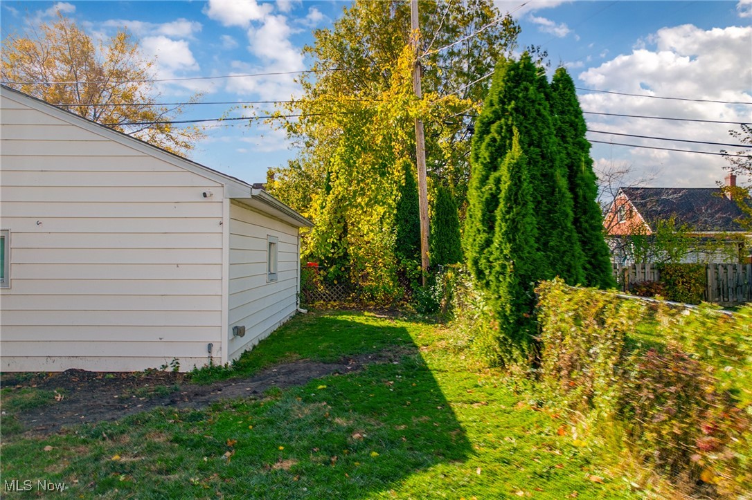 White-sided house beside a grassy yard and tall evergreen hedges in autumn.
