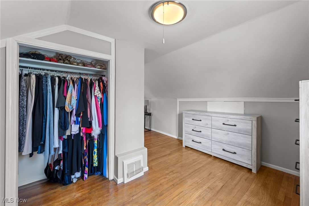 Closet and dressing area with hanging clothes, a gray dresser, hardwood floors, and a sloped ceiling.