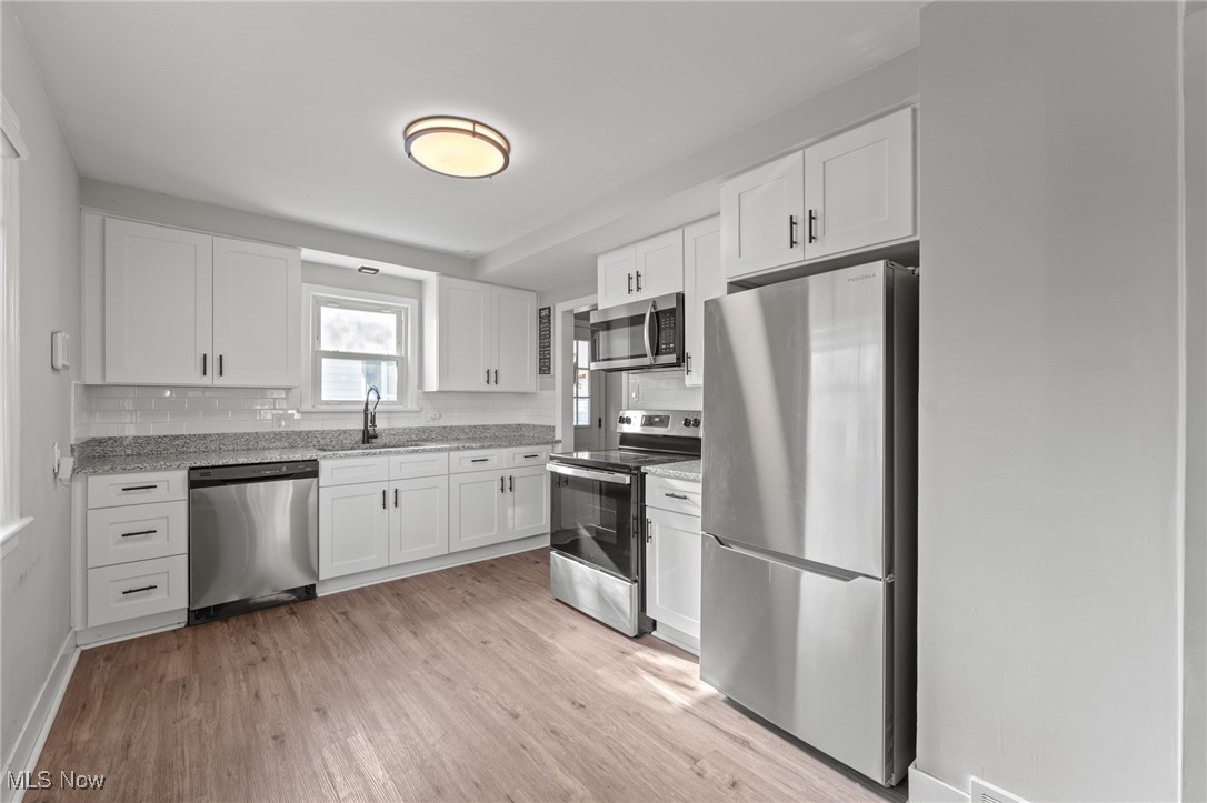 Renovated kitchen with white cabinets, granite counters, stainless steel appliances, and light wood-look flooring.