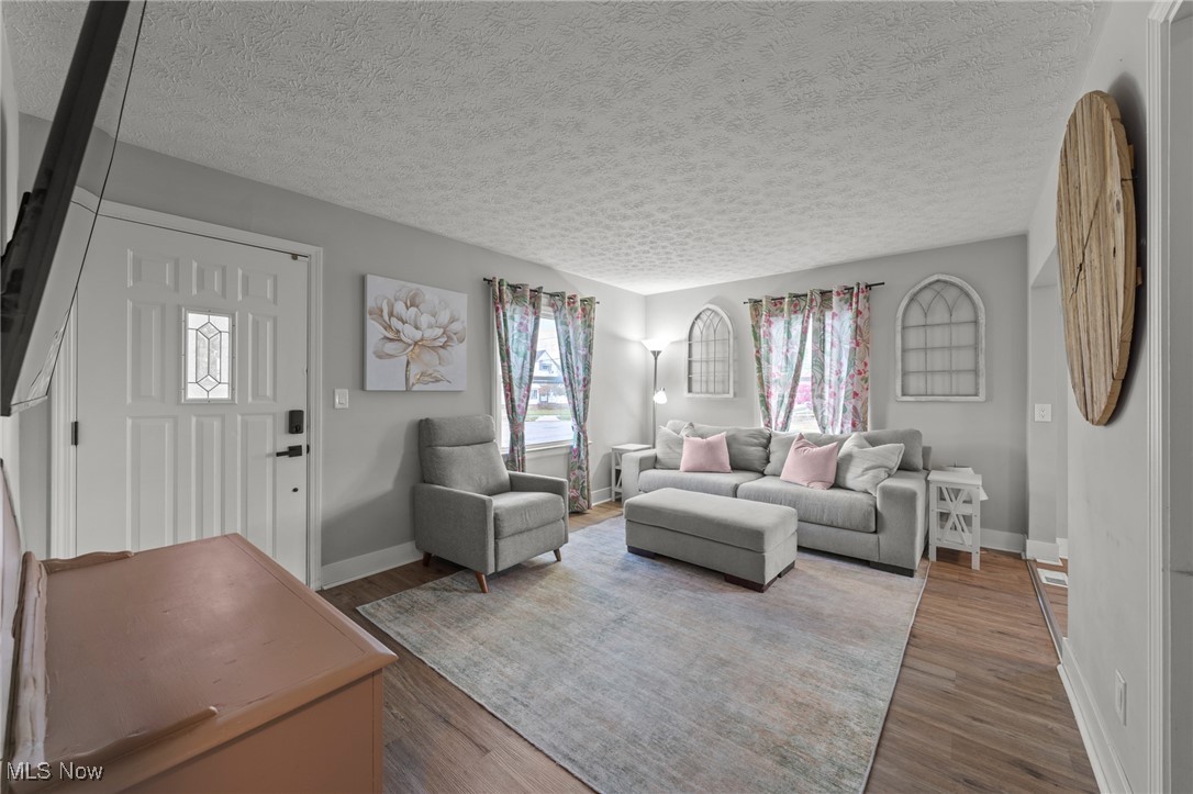 Living room with gray seating, floral curtains, a pale rug and a white paneled front door.