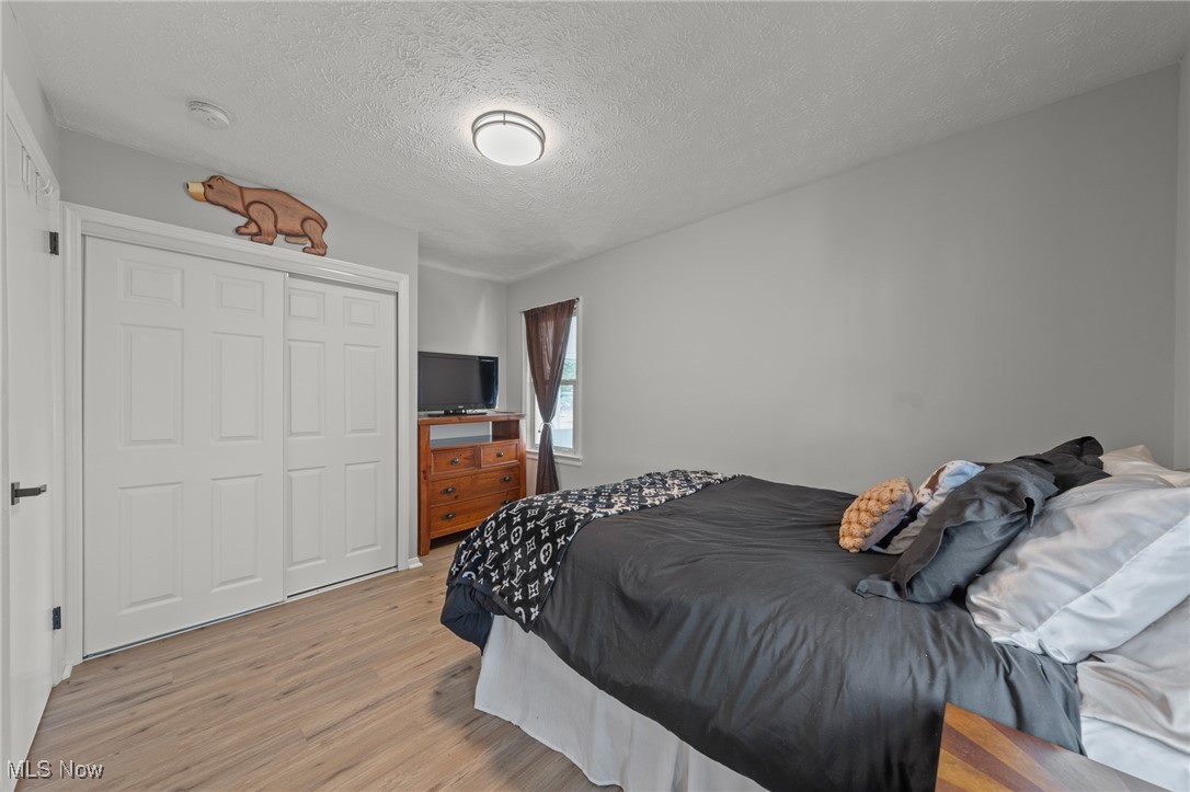 Bedroom with dark bedding, a white sliding closet, and a wooden dresser beside a curtained window.