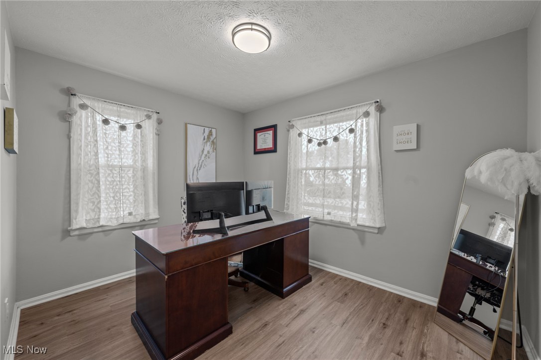 Home office with a dark wood desk, computer monitors, two curtained windows, and a leaning full-length mirror.