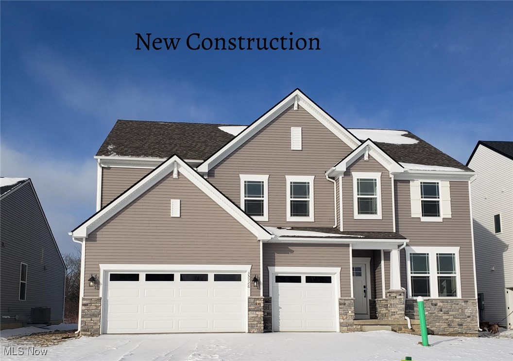 New-construction two-story home with taupe siding, stone accents, and a three-car garage in snow.