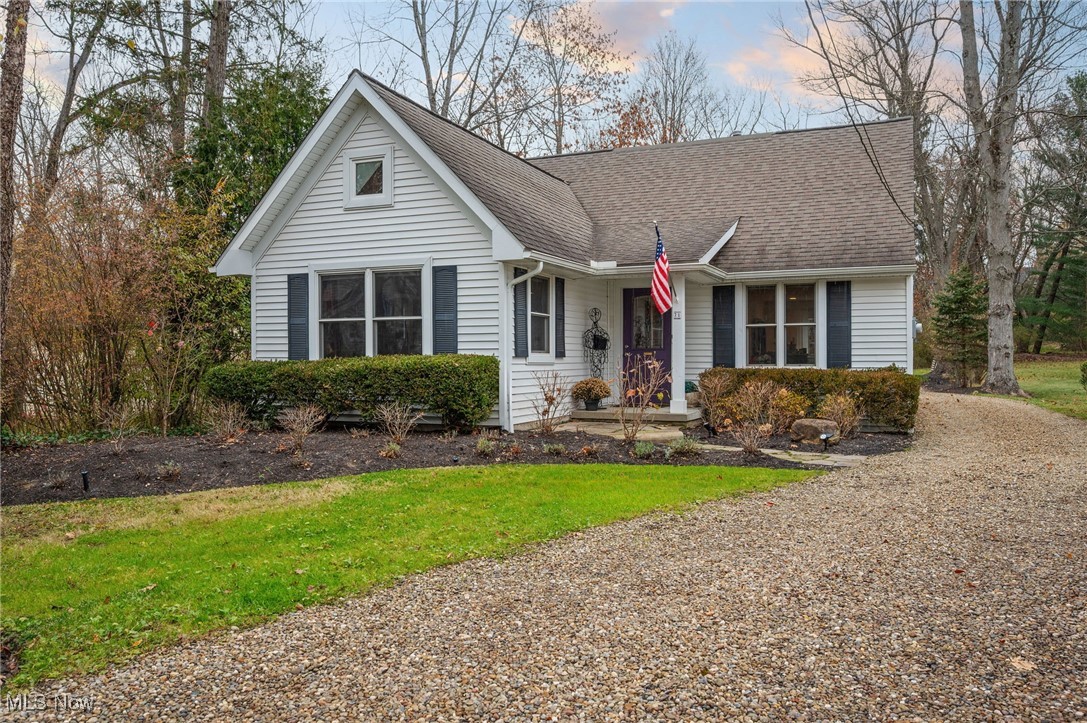 White single-story house with dark shutters, an American flag, and a curving gravel driveway.