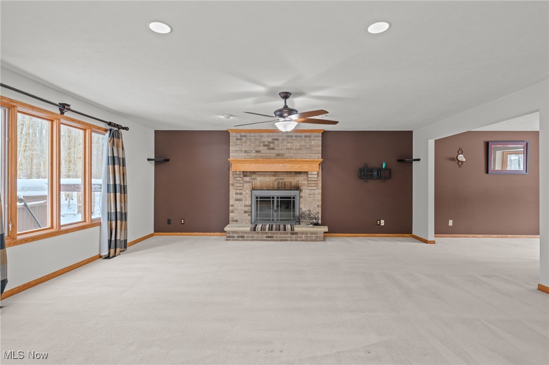 Vacant living room with a brick fireplace, ceiling fan, and large windows overlooking snow.