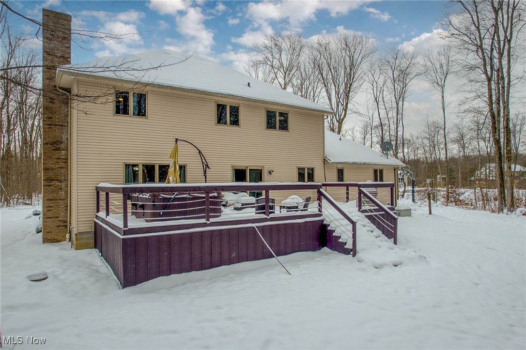 Rear of a beige two-story house with a snow-covered raised deck and tall brick chimney.