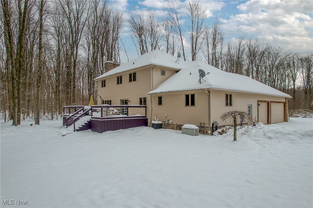 Beige two-story home with an attached garage and purple deck in a snow-covered wooded yard.