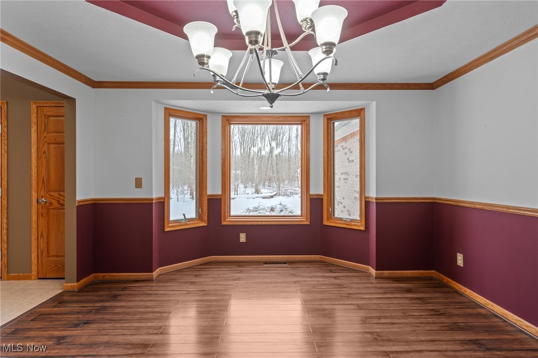 Empty dining room with a wood-trimmed bay window overlooking a snowy yard and a chandelier.