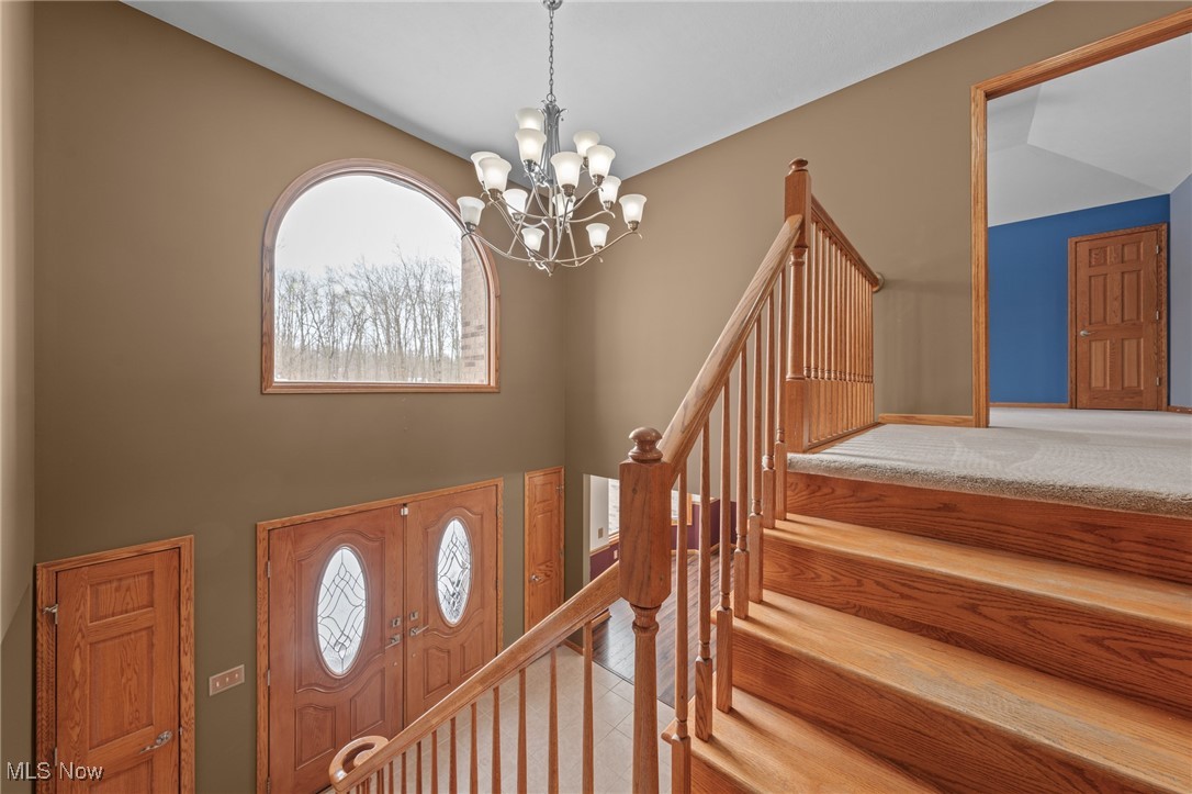 Two-story foyer with a broad wood staircase, arched window, chandelier, and double glass-panel entry doors.