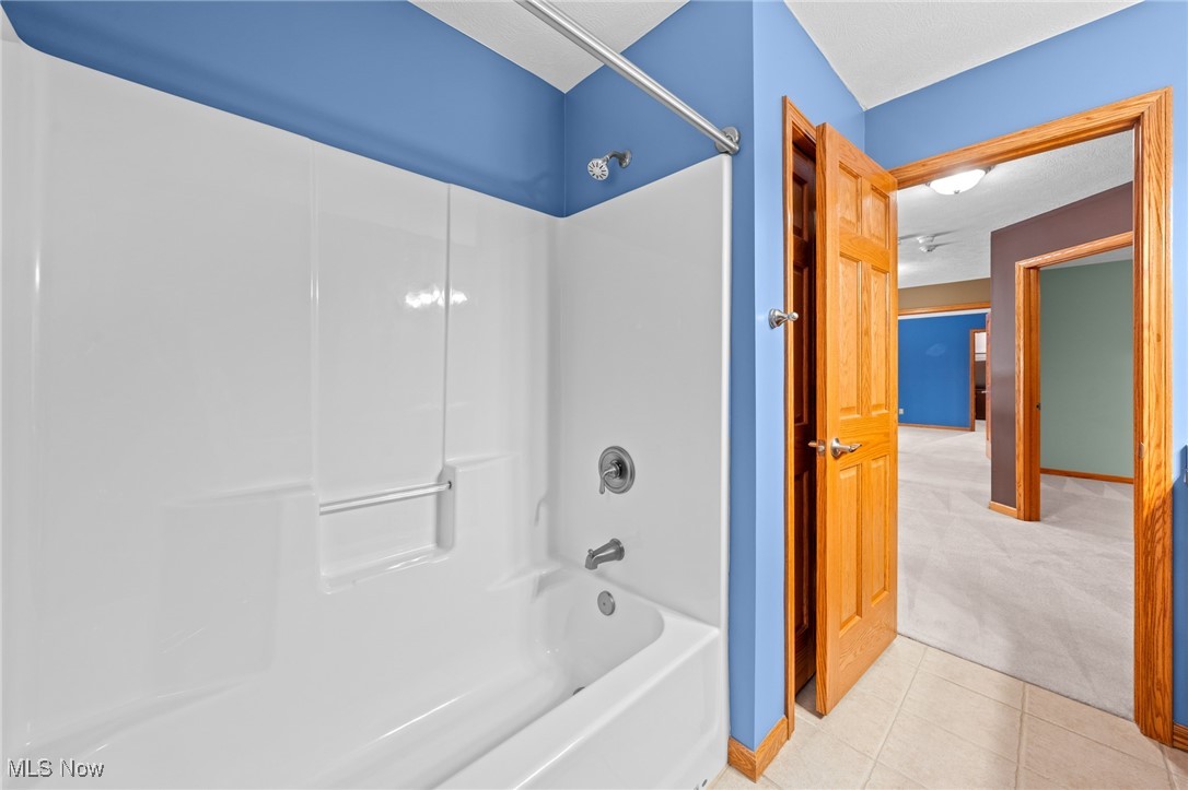 Bathroom with a white tub and shower, blue walls, and an open wooden door to a carpeted hallway.