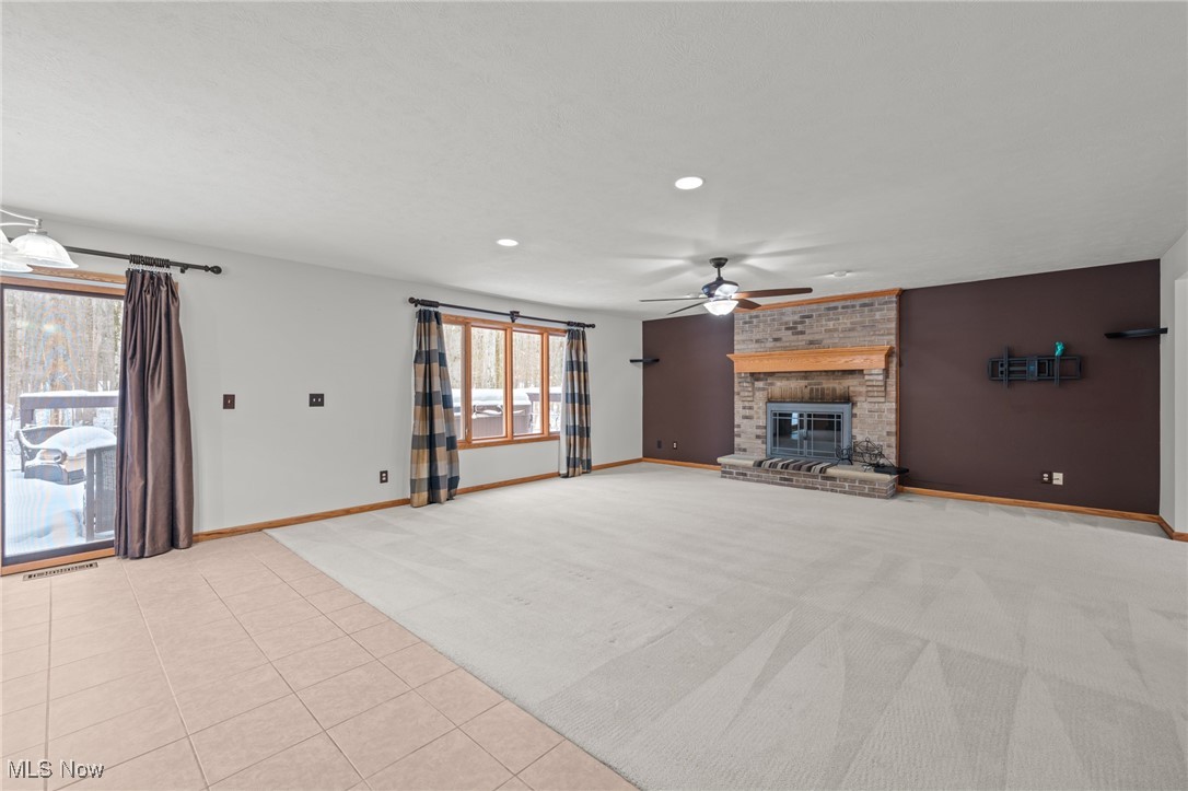 Vacant living room with a brick fireplace, broad carpeted floor, and snowy views through the windows.