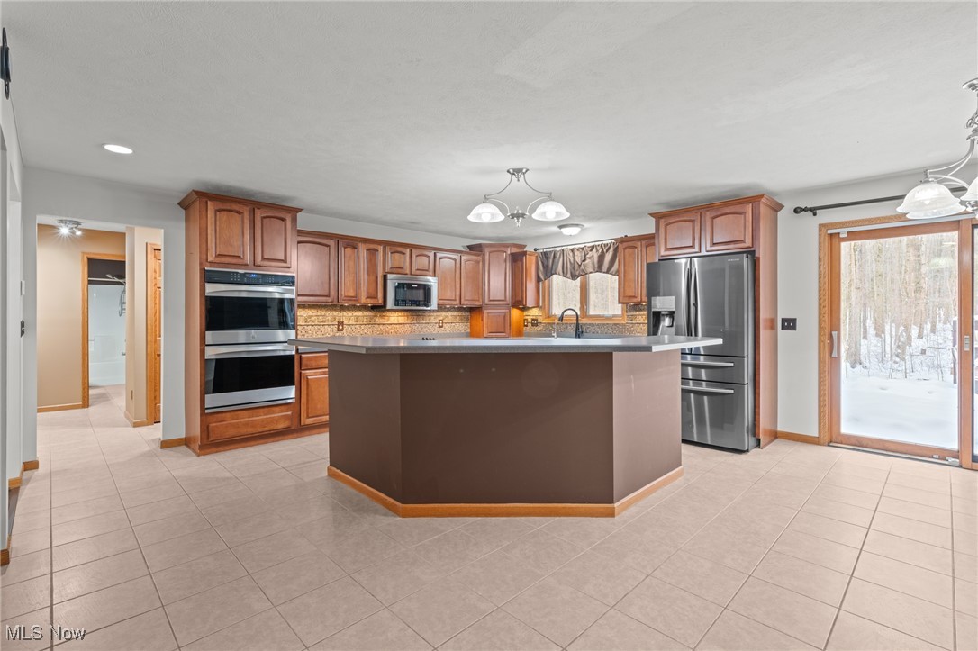 Kitchen with a large island, wood cabinetry, stainless steel appliances, and a sliding door overlooking snowy woods.