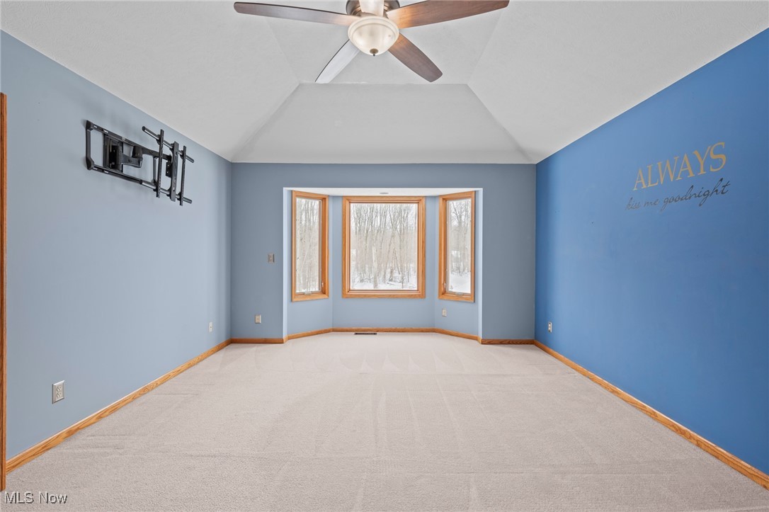 Empty blue bedroom with a bay window overlooking snowy woods and a ceiling fan.