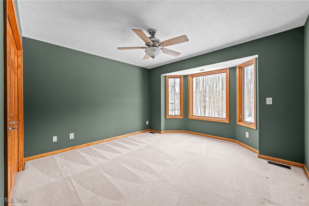 Vacant bedroom with green walls, patterned carpet, and a wood-trimmed bay window.