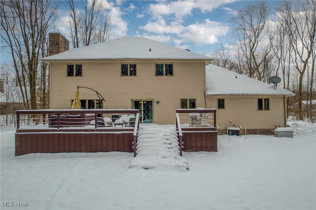 Rear of a beige two-story house with a snow-covered raised deck and yard.